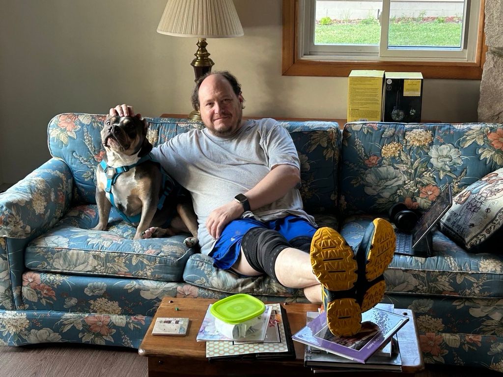 A dog and a person seated on a flowery couch.